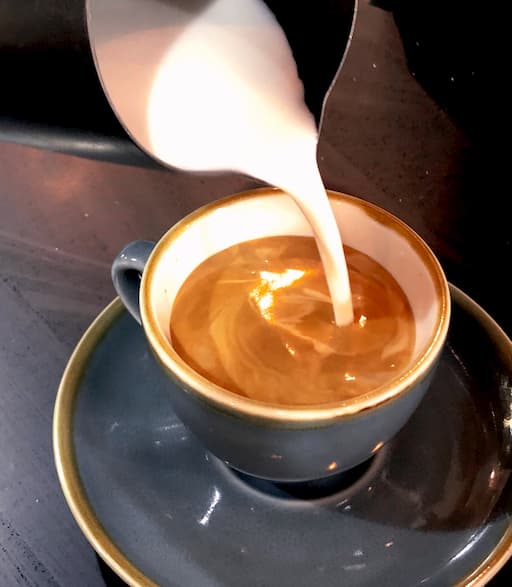 Barista pouring lactose-free steamed milk into a shot of espresso.